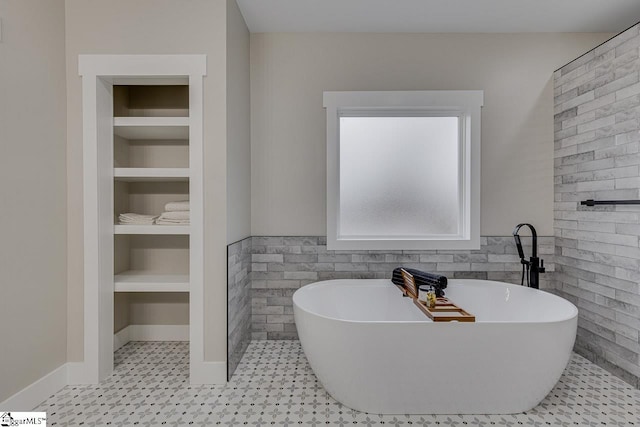 bathroom featuring built in shelves, a bathing tub, tile patterned flooring, and tile walls