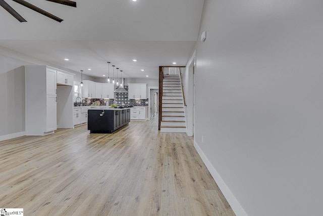 kitchen with tasteful backsplash, decorative light fixtures, a center island, light wood-type flooring, and white cabinets