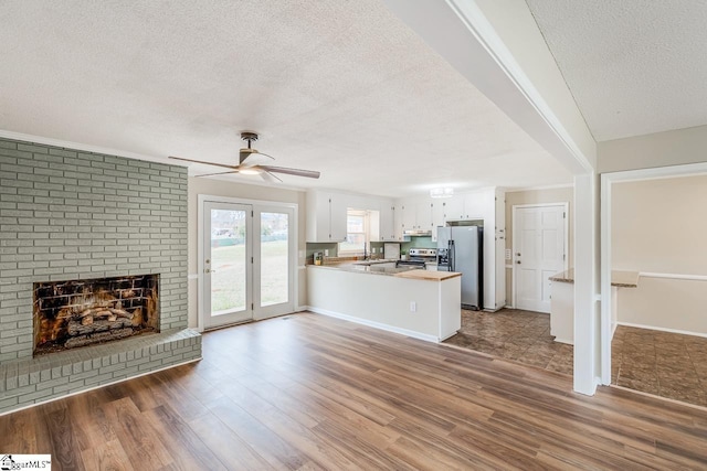 unfurnished living room with a brick fireplace, dark hardwood / wood-style floors, a textured ceiling, and ceiling fan