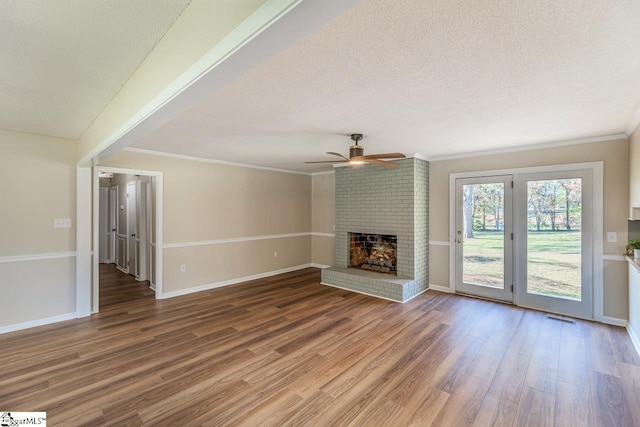 unfurnished living room with a brick fireplace, wood-type flooring, ornamental molding, and a textured ceiling