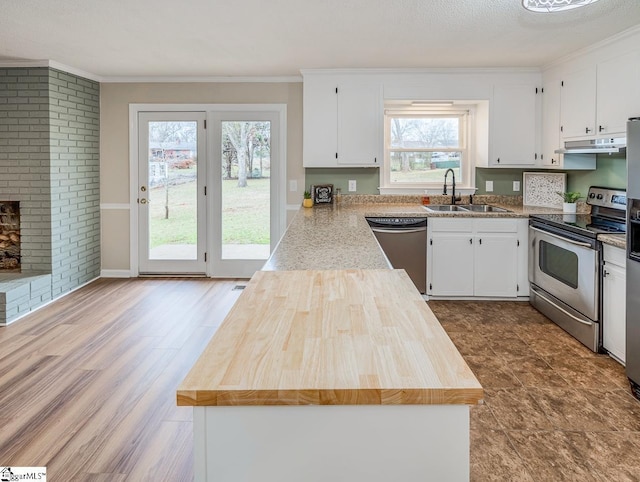 kitchen with sink, stainless steel appliances, ornamental molding, white cabinets, and a brick fireplace