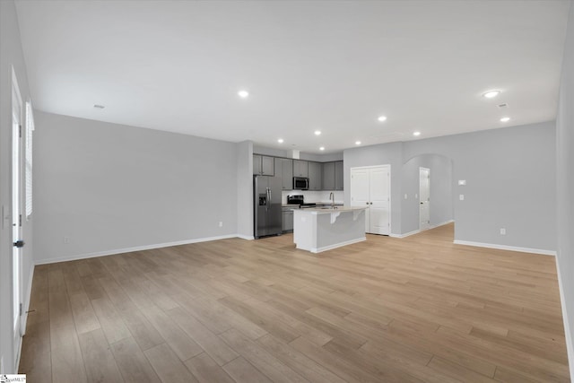 kitchen with a kitchen island with sink, stainless steel appliances, a breakfast bar, and light wood-type flooring