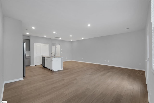 kitchen featuring dishwasher, sink, white cabinets, light hardwood / wood-style floors, and a center island with sink