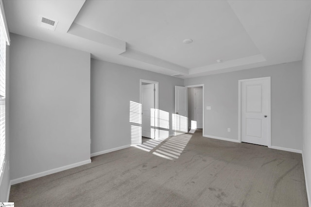 unfurnished room featuring light colored carpet, a tray ceiling, and a wealth of natural light