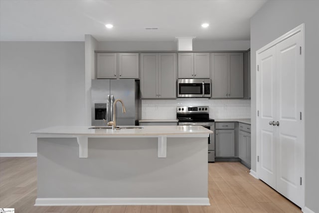 kitchen with gray cabinets, appliances with stainless steel finishes, and a center island with sink