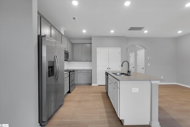 kitchen with stainless steel appliances, sink, a kitchen island with sink, and light hardwood / wood-style flooring