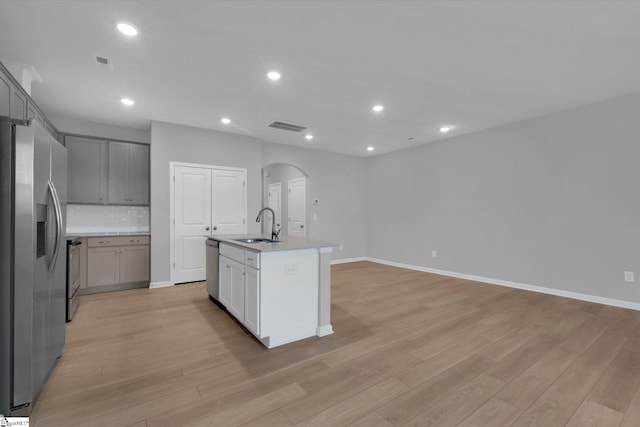 kitchen with sink, light hardwood / wood-style flooring, appliances with stainless steel finishes, gray cabinets, and an island with sink