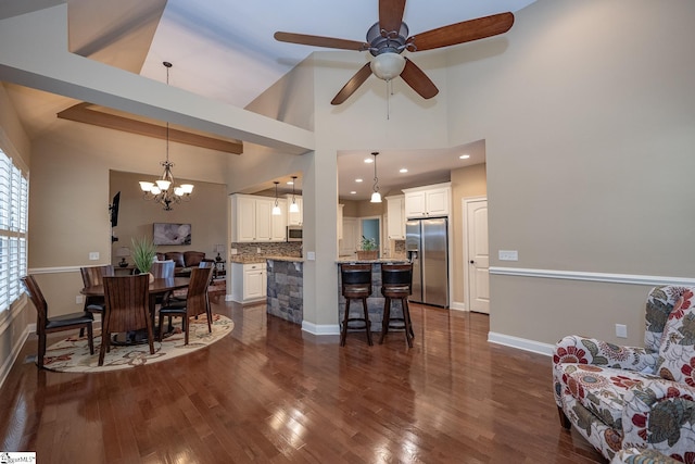 dining space with ceiling fan with notable chandelier, high vaulted ceiling, and dark hardwood / wood-style floors