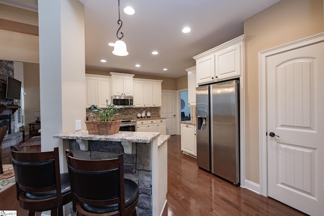 kitchen with a breakfast bar area, light stone counters, kitchen peninsula, stainless steel appliances, and white cabinets