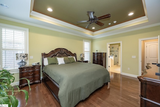 bedroom featuring crown molding, dark wood-type flooring, ceiling fan, ensuite bathroom, and a tray ceiling