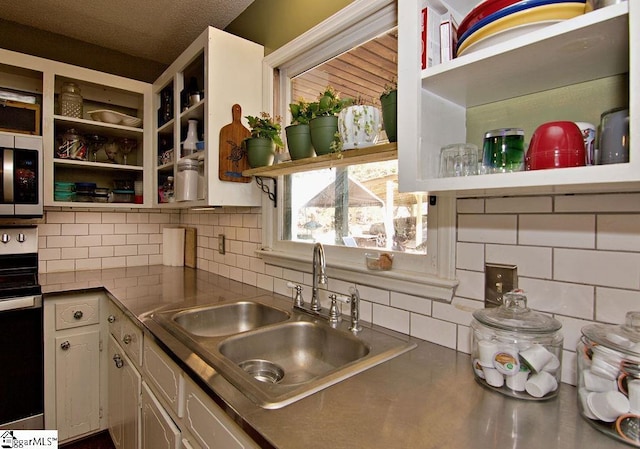 kitchen with white cabinetry, stove, sink, and decorative backsplash