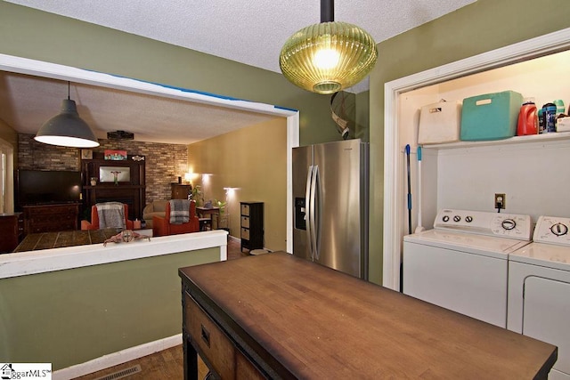 kitchen featuring stainless steel refrigerator with ice dispenser, a textured ceiling, washing machine and clothes dryer, a brick fireplace, and decorative light fixtures