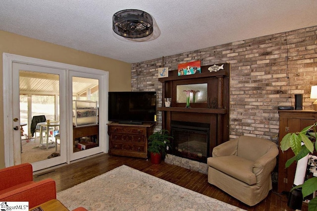 living area with a fireplace, dark hardwood / wood-style floors, a textured ceiling, and brick wall