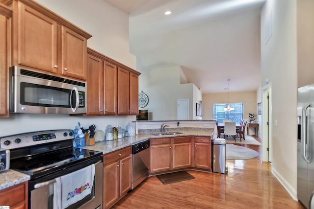 kitchen with pendant lighting, sink, light hardwood / wood-style flooring, stainless steel appliances, and light stone countertops