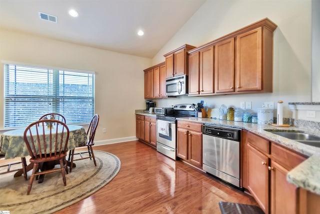 kitchen with vaulted ceiling, appliances with stainless steel finishes, sink, light stone countertops, and light wood-type flooring