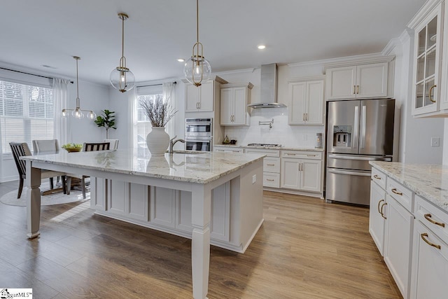 kitchen with appliances with stainless steel finishes, a breakfast bar, an island with sink, hanging light fixtures, and wall chimney exhaust hood