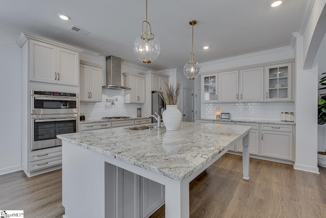 kitchen featuring a large island, sink, stainless steel appliances, decorative light fixtures, and wall chimney exhaust hood