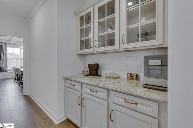 bar with crown molding, white cabinetry, light stone counters, decorative backsplash, and light wood-type flooring