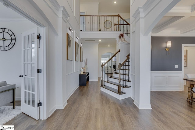 foyer featuring ornamental molding, a towering ceiling, and light wood-type flooring