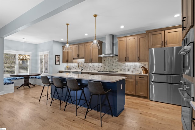 kitchen featuring stainless steel appliances, a center island, a kitchen bar, decorative light fixtures, and wall chimney exhaust hood