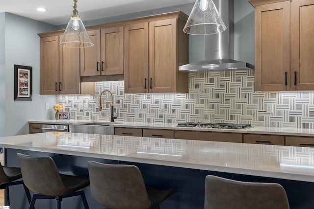 kitchen with pendant lighting, sink, a kitchen bar, stainless steel appliances, and wall chimney range hood