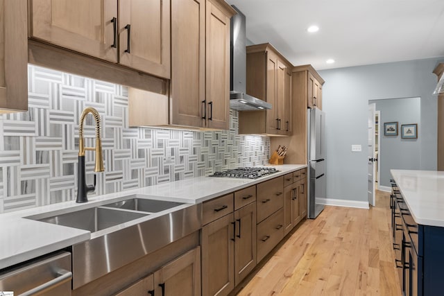 kitchen featuring wall chimney range hood, sink, stainless steel appliances, light hardwood / wood-style floors, and decorative backsplash