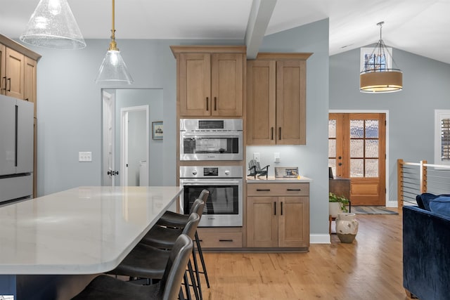 kitchen featuring stainless steel appliances, decorative light fixtures, a breakfast bar area, and light wood-type flooring