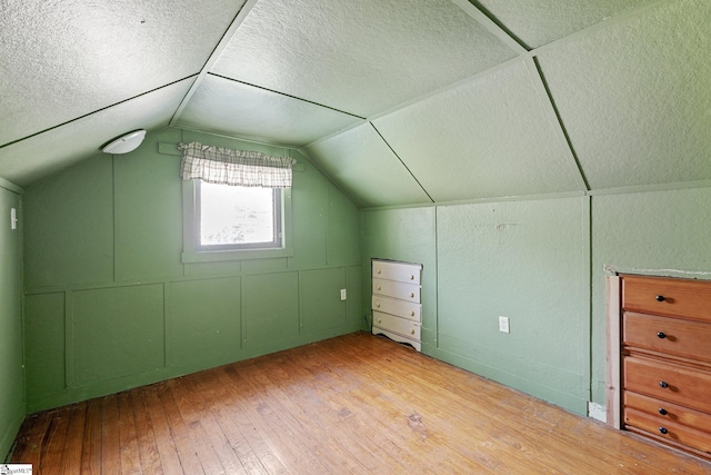 additional living space featuring vaulted ceiling, a textured ceiling, and light hardwood / wood-style flooring