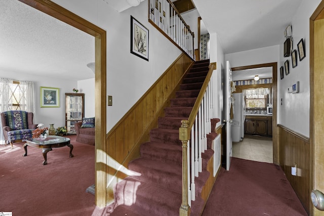 stairs with plenty of natural light, wood walls, a textured ceiling, and carpet flooring