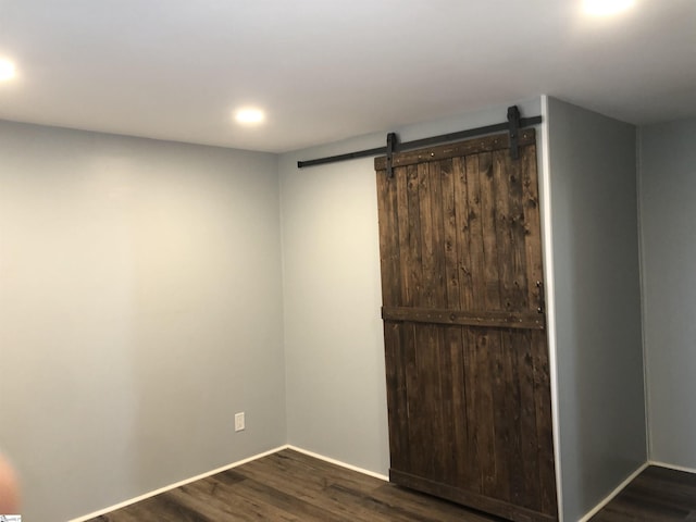 empty room with a barn door and dark wood-type flooring