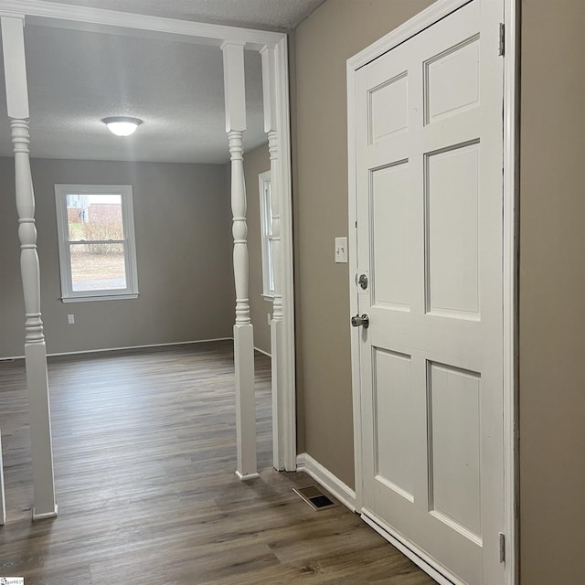 foyer entrance featuring ornate columns, dark wood-type flooring, and a textured ceiling