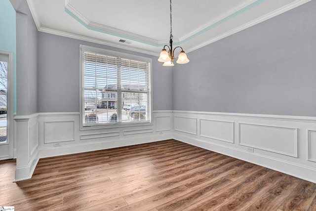 unfurnished dining area with hardwood / wood-style flooring, crown molding, a raised ceiling, and a chandelier