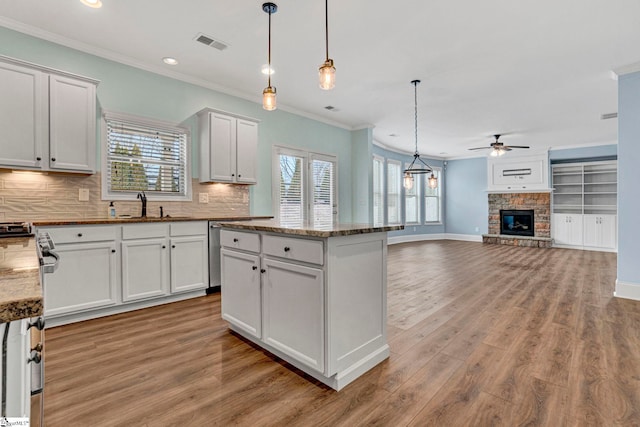 kitchen with sink, white cabinetry, light stone counters, decorative light fixtures, and a center island