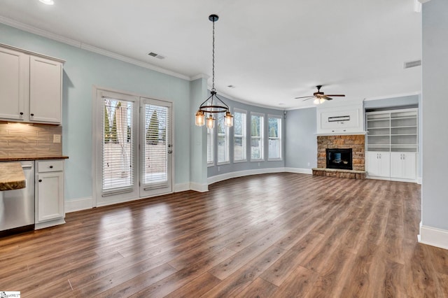 unfurnished living room featuring a stone fireplace, ceiling fan with notable chandelier, ornamental molding, and dark hardwood / wood-style floors