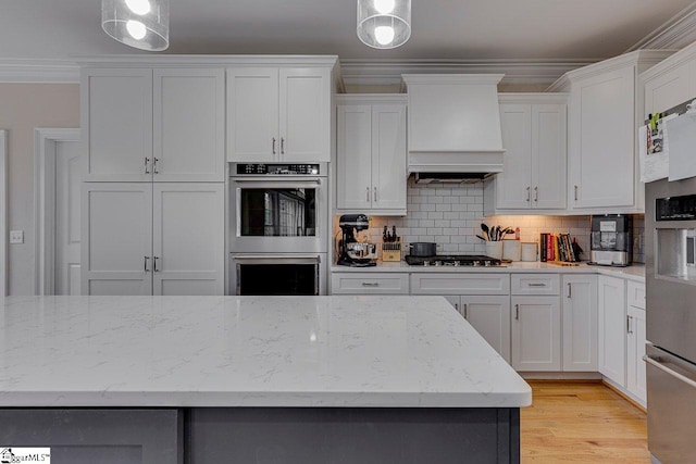 kitchen featuring white cabinetry, decorative light fixtures, custom exhaust hood, and appliances with stainless steel finishes