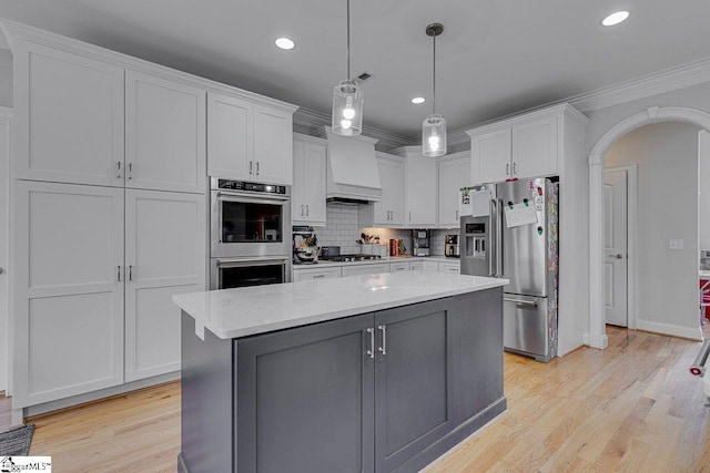 kitchen featuring premium range hood, white cabinetry, appliances with stainless steel finishes, a center island, and light stone countertops