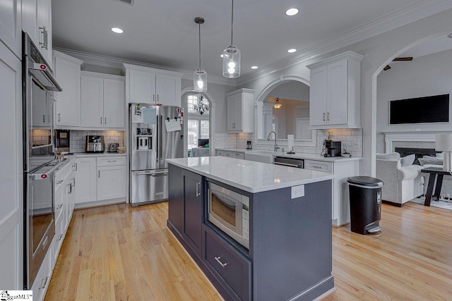 kitchen featuring crown molding, a center island, hanging light fixtures, appliances with stainless steel finishes, and white cabinets