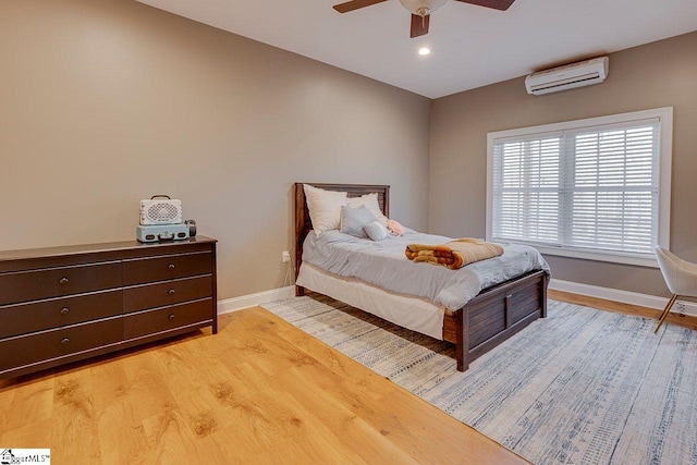 bedroom with a wall mounted AC, ceiling fan, and light hardwood / wood-style flooring