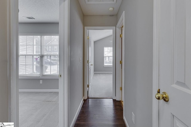 hallway with a textured ceiling and dark colored carpet