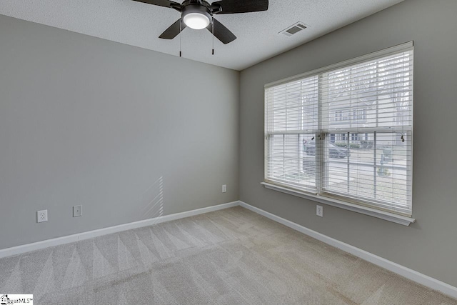 unfurnished room featuring light carpet, ceiling fan, a textured ceiling, and a healthy amount of sunlight