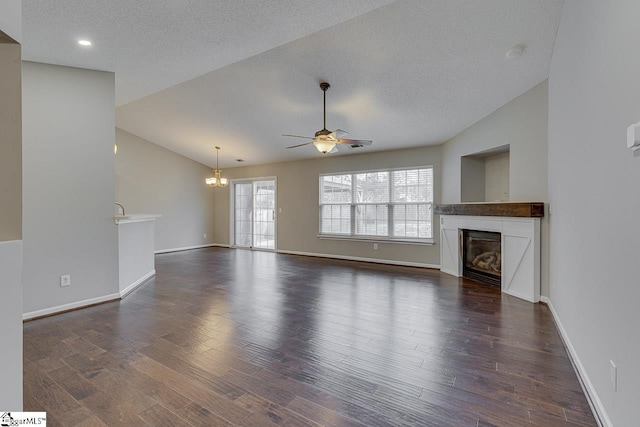 unfurnished living room featuring lofted ceiling, ceiling fan with notable chandelier, a fireplace, and dark hardwood / wood-style floors