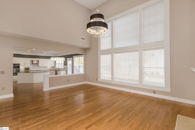 unfurnished living room featuring a high ceiling, light hardwood / wood-style flooring, and a notable chandelier