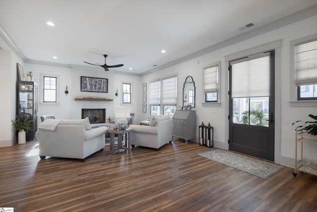 living room with a fireplace, dark wood-type flooring, ornamental molding, and ceiling fan