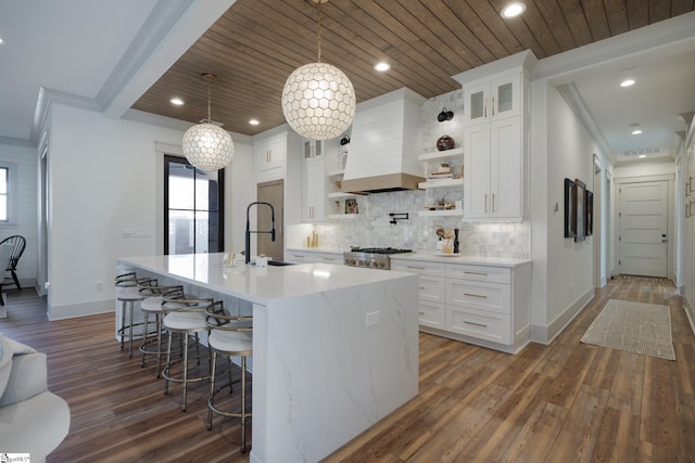 kitchen featuring premium range hood, sink, decorative light fixtures, an island with sink, and white cabinets