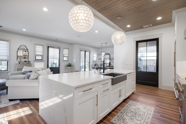 kitchen with pendant lighting, an island with sink, sink, white cabinets, and a notable chandelier