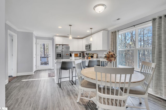 dining room with ornamental molding, sink, light wood-type flooring, and a wealth of natural light