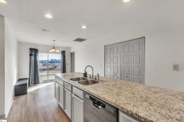 kitchen featuring sink, dishwasher, light hardwood / wood-style floors, a textured ceiling, and decorative light fixtures