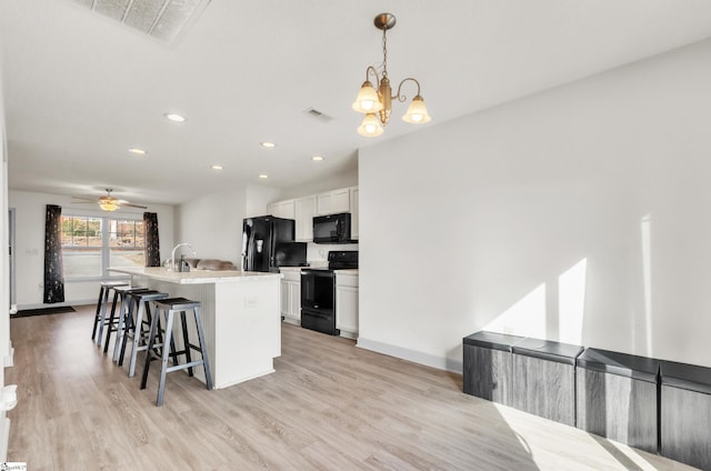 kitchen featuring a breakfast bar area, decorative light fixtures, black appliances, a kitchen island with sink, and white cabinets