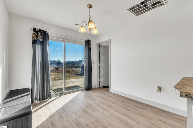 spare room featuring an inviting chandelier, light hardwood / wood-style floors, and a textured ceiling