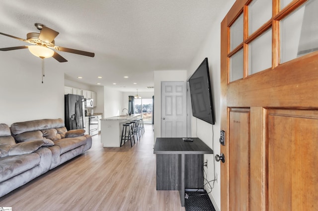 living room featuring ceiling fan, a textured ceiling, and light wood-type flooring